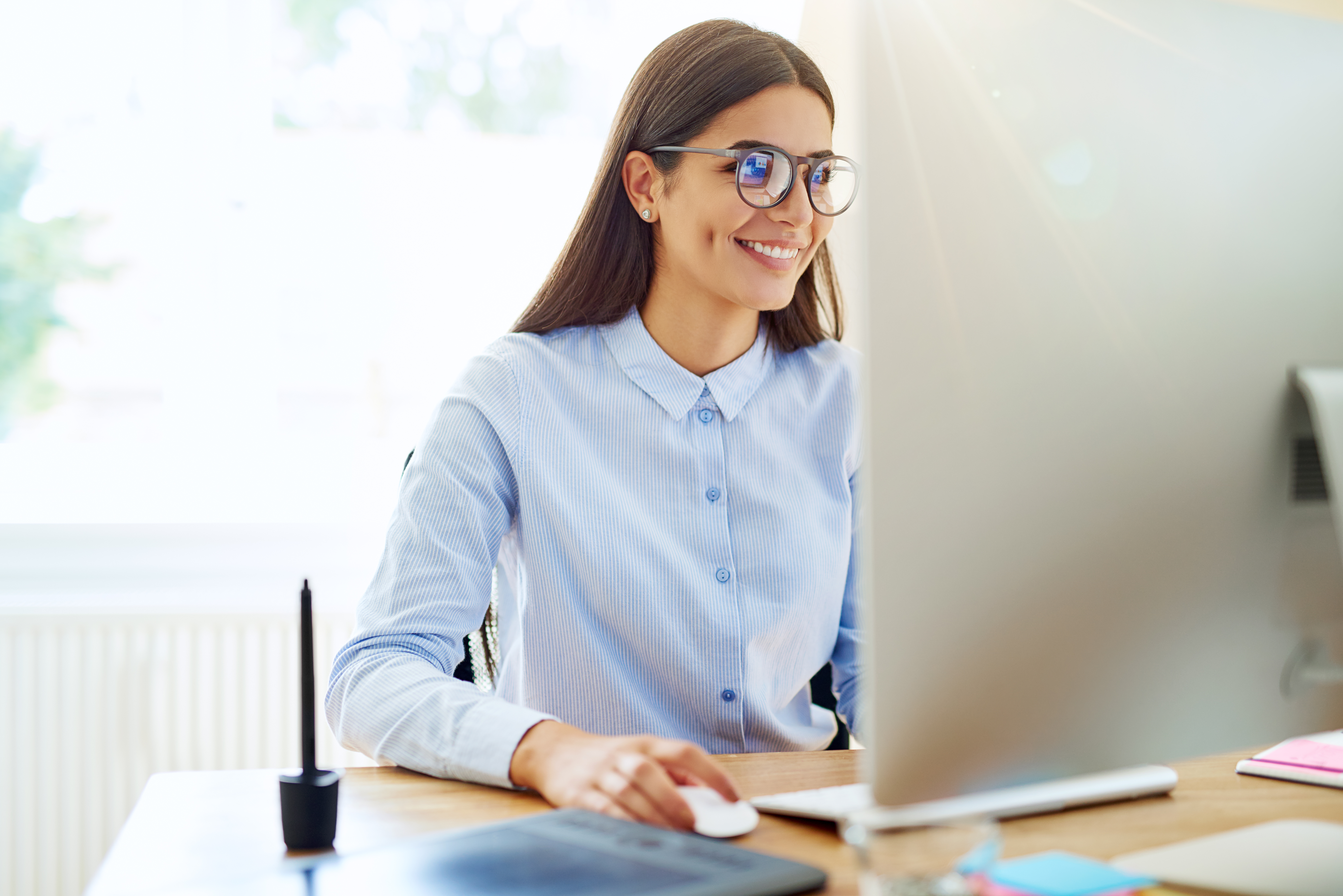Woman with glasses smiling staring at a computer screen