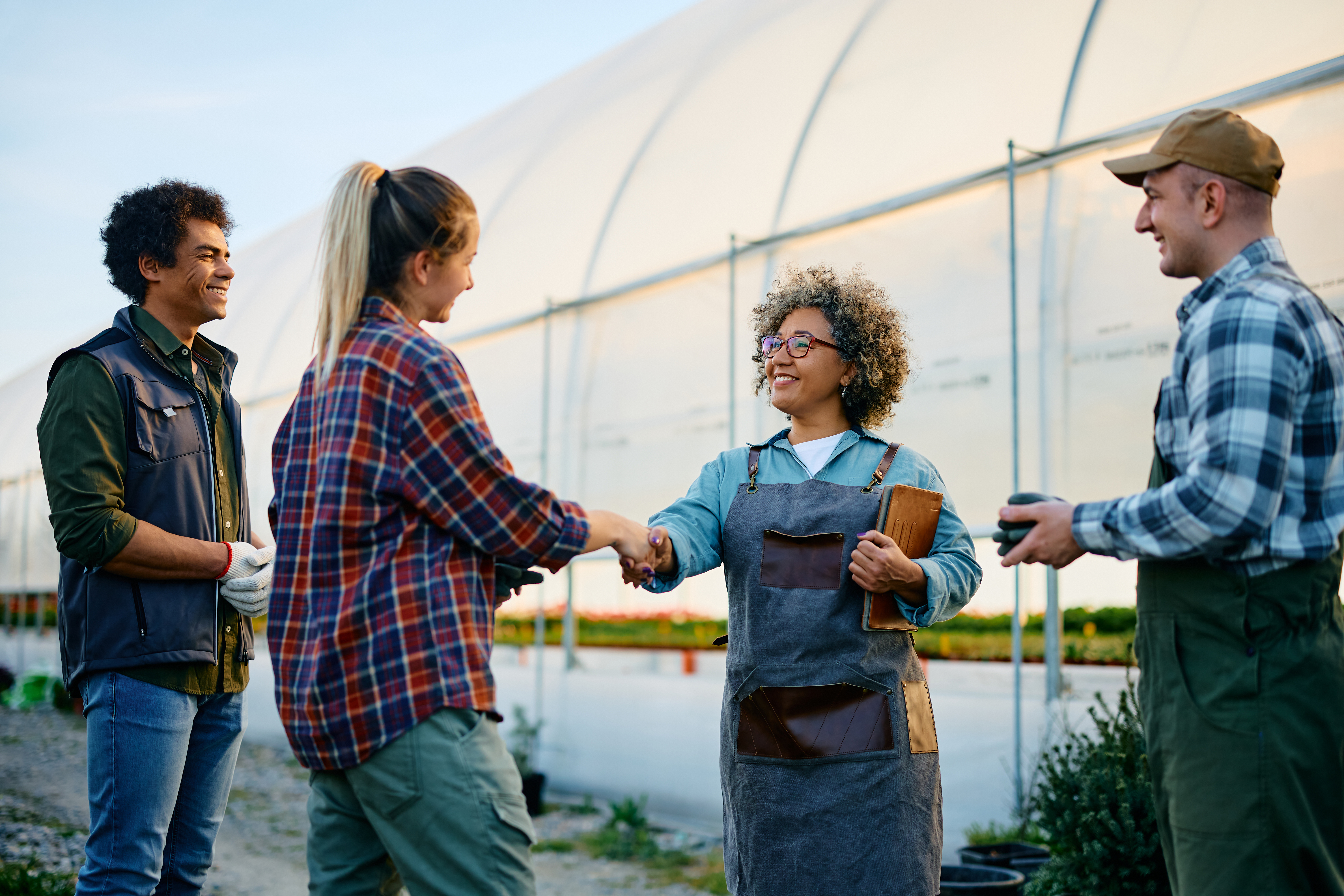 Agricultural workers shake hands in front of a greenhouse